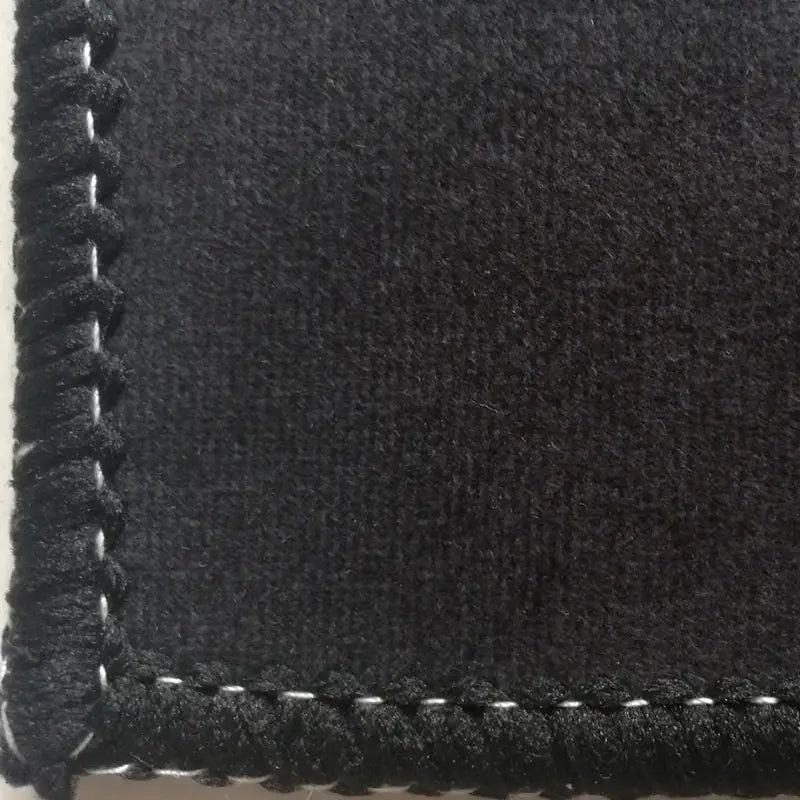 Gros plan sur un tapis de sol personnalisé en tissu noir avec surpiqûres, portant les noms d’un chien et d’un chat
